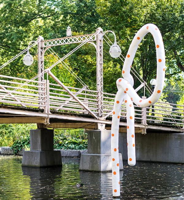Image of sculpture of large polkadot rope emerging from river and tied in a knot