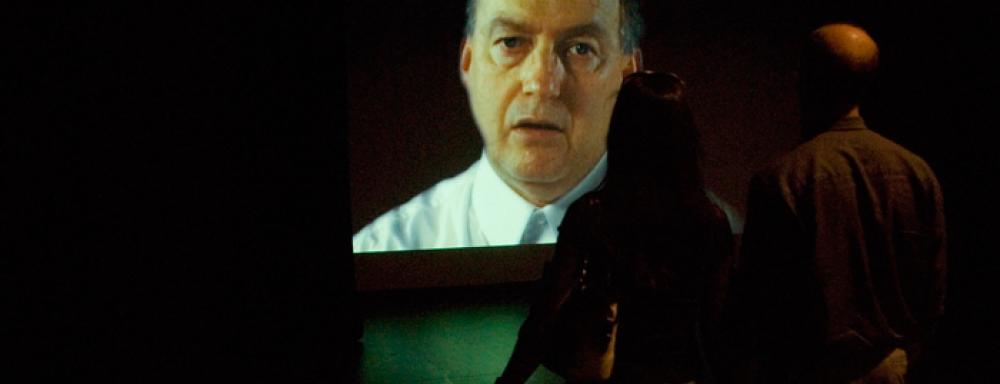 a couple standing in front of a projection of a man speaking.